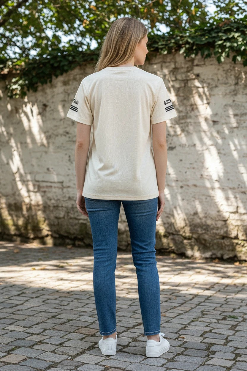 The Nile Luxuries cream moisture-wicking performance t-shirt with micro-mesh texture and sleeve stripes worn by a woman