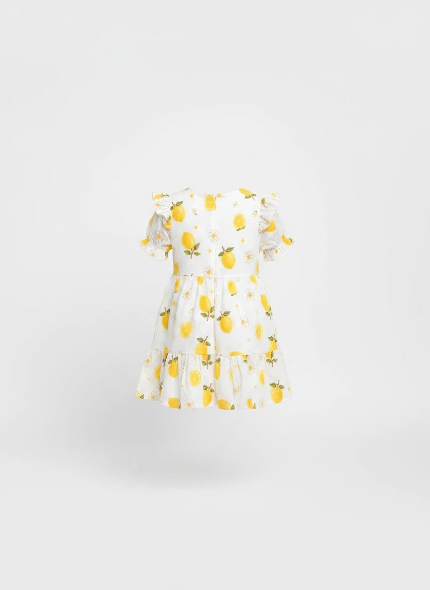 The Nile Luxuries girls white dress with yellow lemon and daisy print, featuring puff sleeves and a tiered skirt.