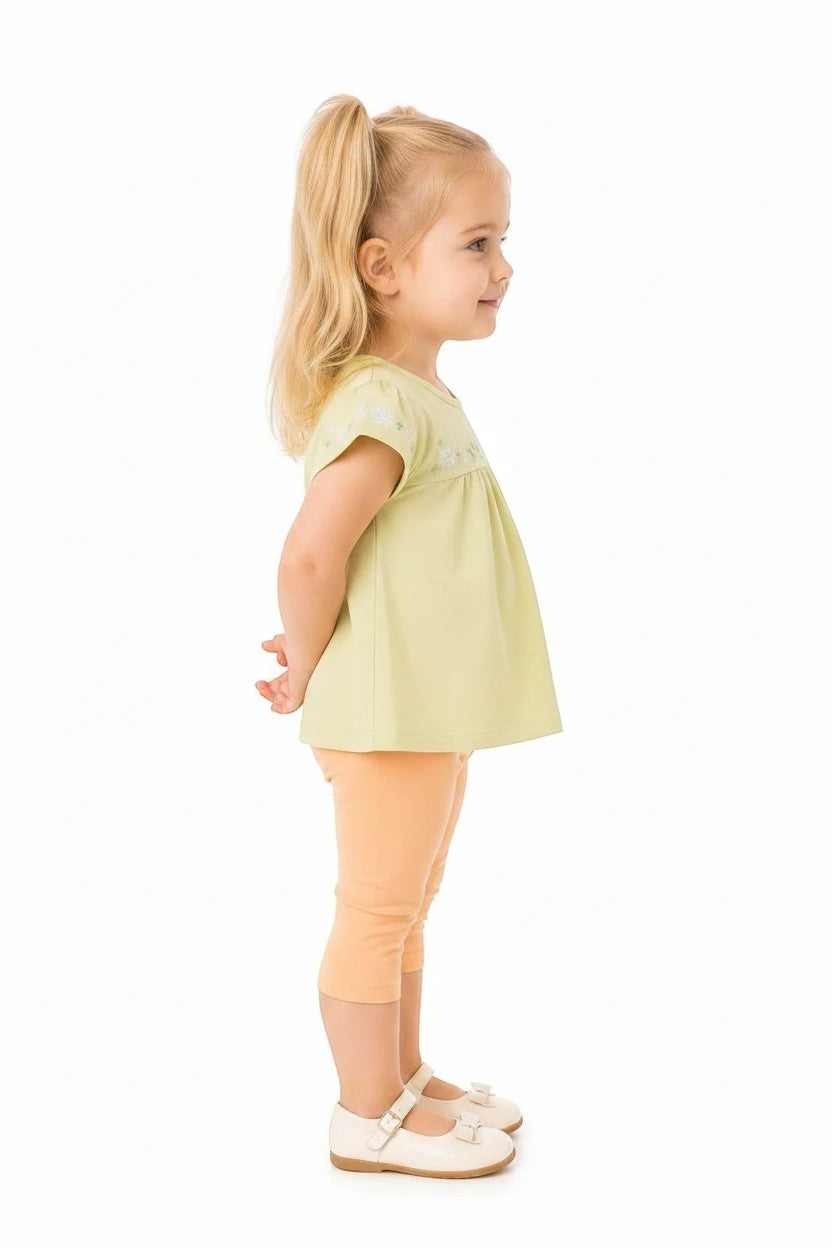 Toddler girl wearing The Nile Luxuries floral embroidered lime top and peach capri leggings on a white background.