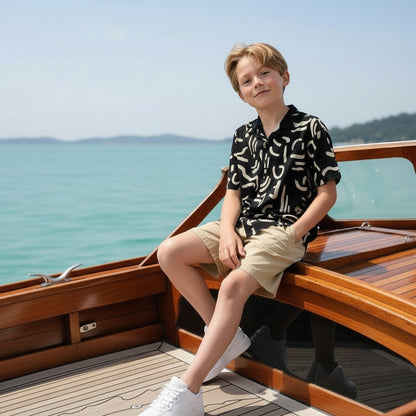 The Nile Luxuries black short sleeve shirt with abstract white print, worn by a boy on a boat.