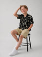 The Nile Luxuries black short sleeve shirt with abstract print, collared neckline, worn by a boy sitting on a stool.