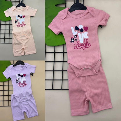 The Nile Luxuries baby ribbed knit bodysuit and shorts set in peach, pink, and lavender. Short-sleeved onesie with "LOVE and Laugh" graphic.