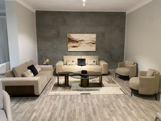 The Nile Luxuries modern beige fabric sofa set with accent chairs, coffee table, and side table. Features wooden detailing and plush cushions.
