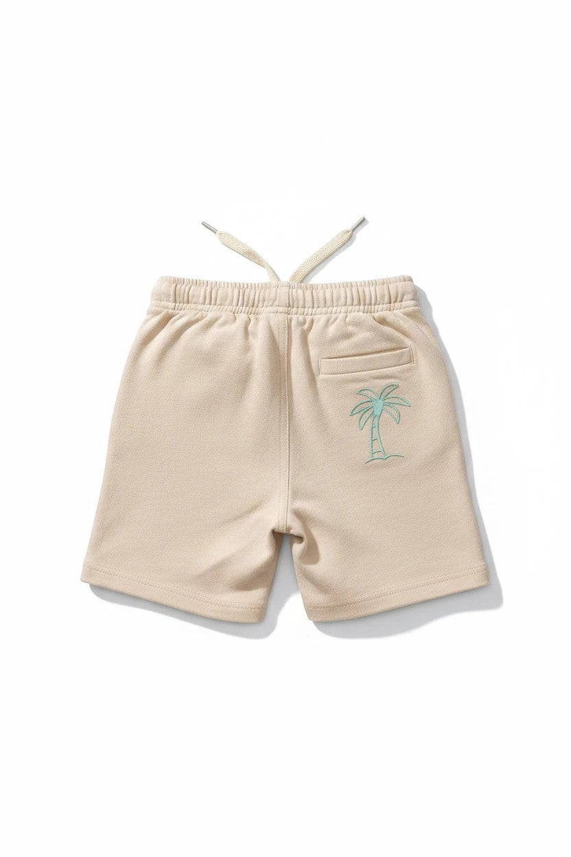 The Nile Luxuries beige cotton shorts with an elastic drawstring waistband and sage green palm tree embroidery.