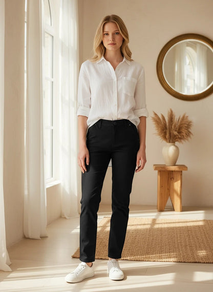 The Nile Luxuries classic black chino trousers worn by a woman with a white button-down shirt and white sneakers.