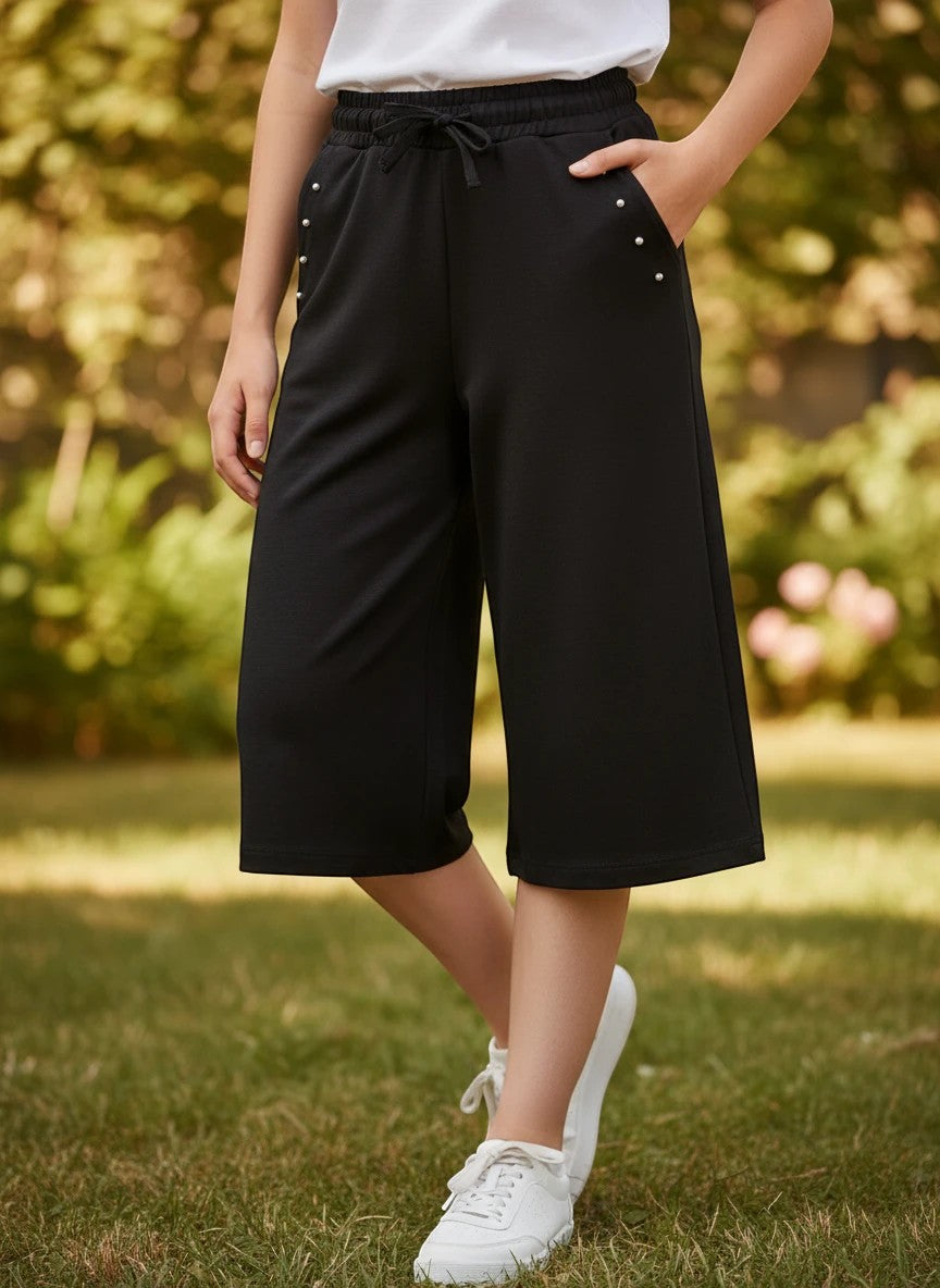 The Nile Luxuries girls black culotte pants with drawstring waist, side pockets, and delicate stud embellishments.