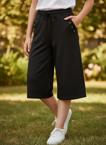 The Nile Luxuries girls black culotte pants with drawstring waist, side pockets, and delicate stud embellishments.