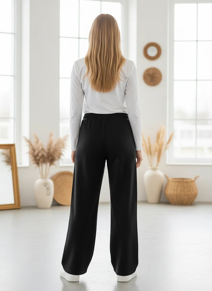 The Nile Luxuries black wide-leg lounge pants with an elastic drawstring waist worn by a woman from the back view.