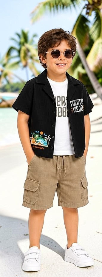 The Nile Luxuries Boys black short sleeve camp shirt with tropical graphic and PUERTO VIEJO lettering, paired with khaki cargo shorts.