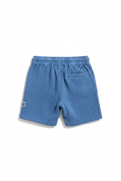 The Nile Luxuries boys blue gauze shorts with elastic waistband and pocket. Features a small grey patch with 'LP' logo.