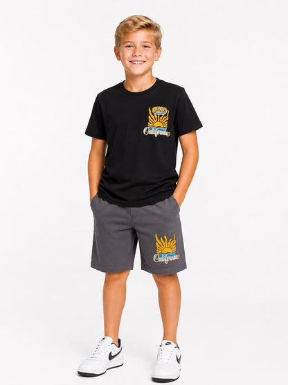 A young boy wearing a black The Nile Luxuries California graphic t-shirt and grey cotton shorts set.