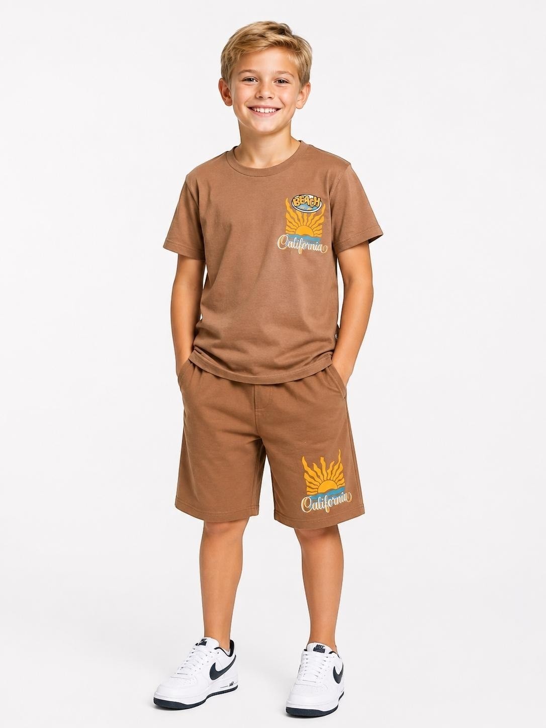 A smiling boy wearing a brown The Nile Luxuries cotton t-shirt and shorts set with a retro California beach graphic.