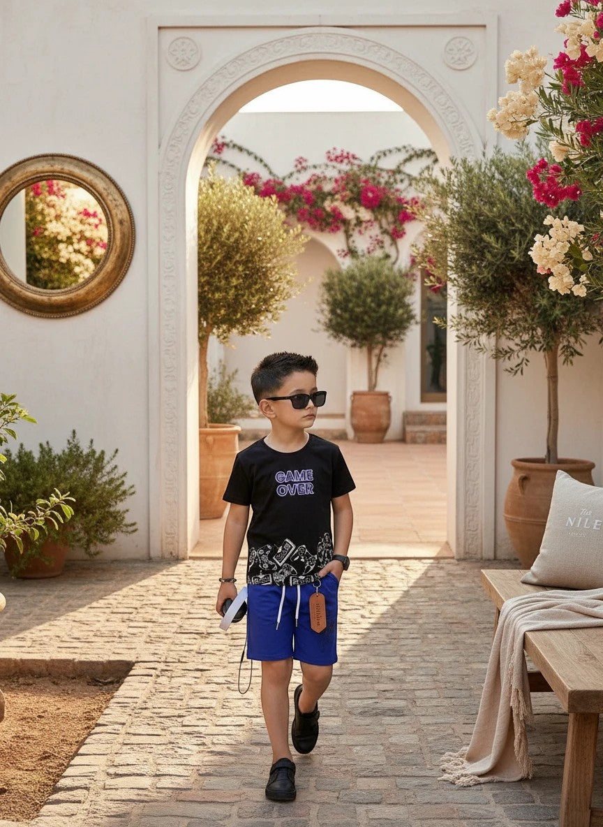 The Nile Luxuries boys black Game Over graphic t-shirt and blue drawstring shorts outfit set worn by a young boy.