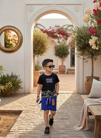 The Nile Luxuries boys black Game Over graphic t-shirt and blue drawstring shorts outfit set worn by a young boy.