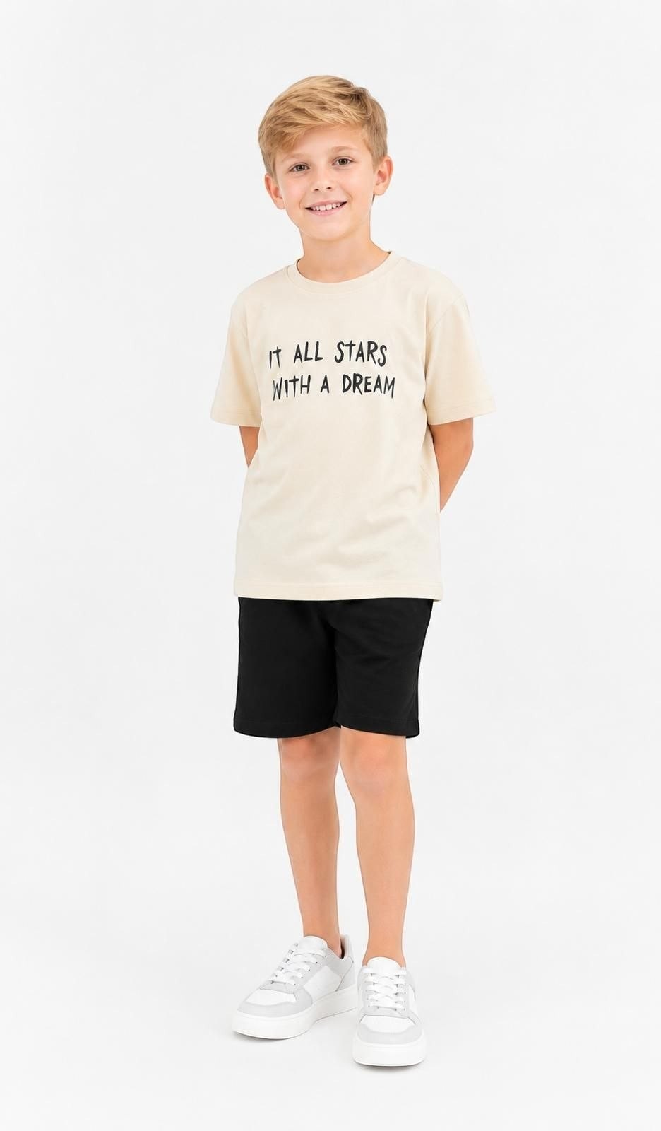Boy wearing The Nile Luxuries beige cotton t-shirt with It All Starts With A Dream graphic print and black shorts.