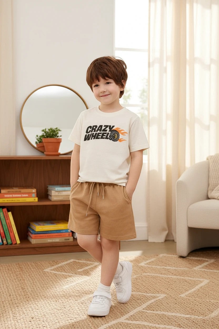 The Nile Luxuries boys outfit with a cream Crazy Wheels graphic t-shirt and tan drawstring shorts in a living room.