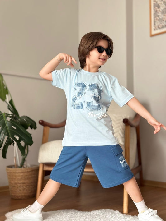 The Nile Luxuries boys light blue graphic t-shirt and dark blue cargo shorts set worn by a boy with sunglasses.