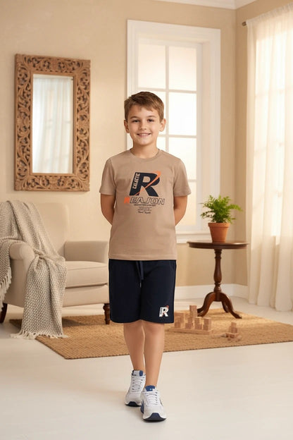 A young boy wearing a The Nile Luxuries beige graphic t-shirt and navy blue athletic shorts in a bright living room.