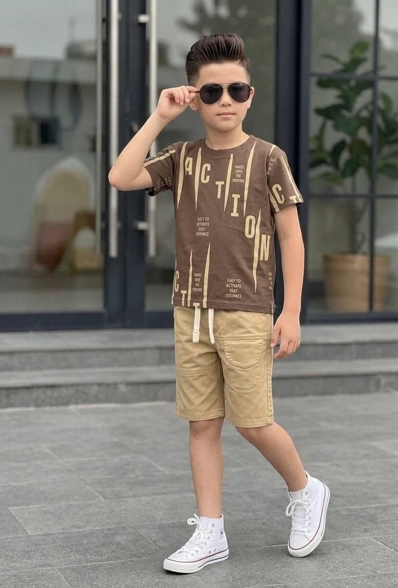 Boy wearing The Nile Luxuries brown graphic t-shirt and beige shorts with white sneakers and sunglasses outdoors.