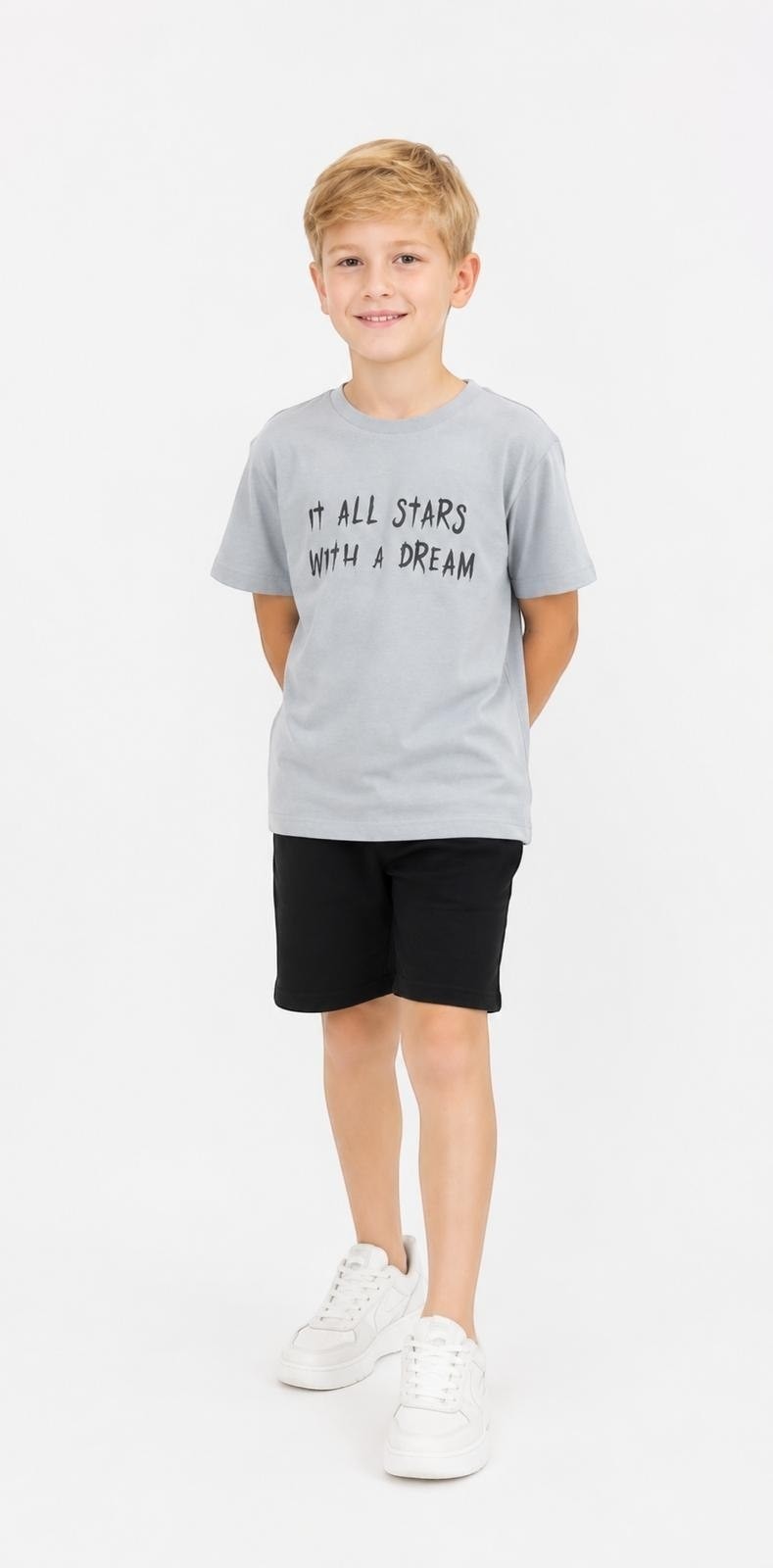 A boy wearing a grey The Nile Luxuries graphic t-shirt with the text It All Starts With A Dream and black shorts.