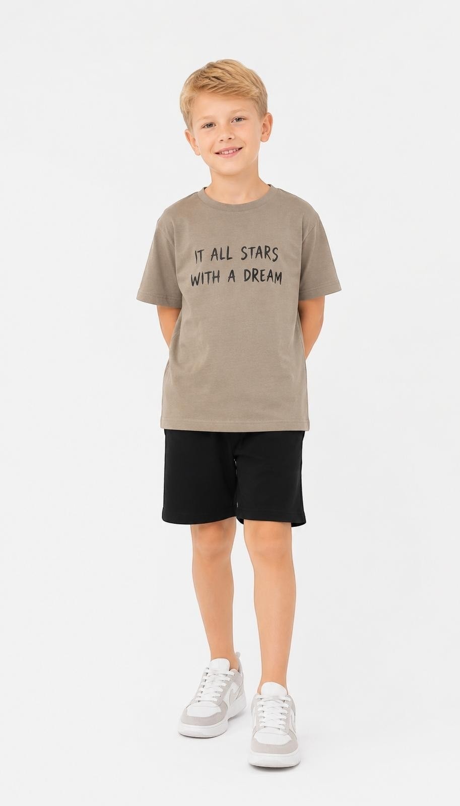 A boy wearing a The Nile Luxuries taupe graphic t-shirt with the text It All Starts With A Dream and black shorts.