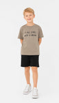 A boy wearing a The Nile Luxuries taupe graphic t-shirt with the text It All Starts With A Dream and black shorts.