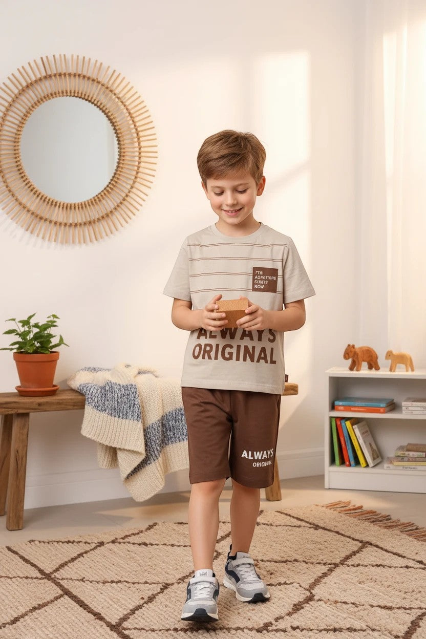 A boy wearing a The Nile Luxuries beige striped graphic t-shirt and brown shorts set in a bright, modern bedroom.