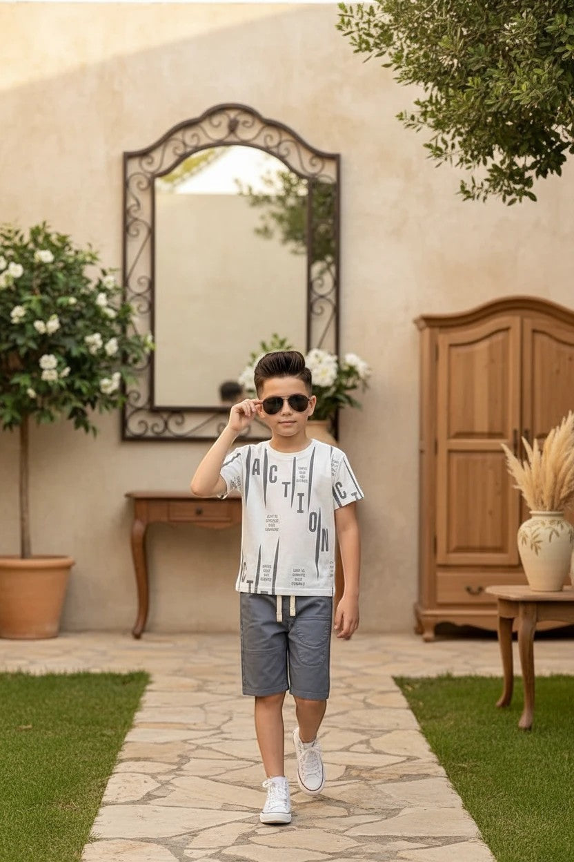 Boy wearing The Nile Luxuries graphic t-shirt and grey shorts with white sneakers in a garden setting.