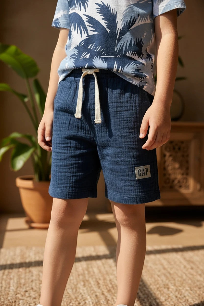 The Nile Luxuries boys' navy gauze shorts with drawstring and GAP logo patch, paired with a palm tree print t-shirt.
