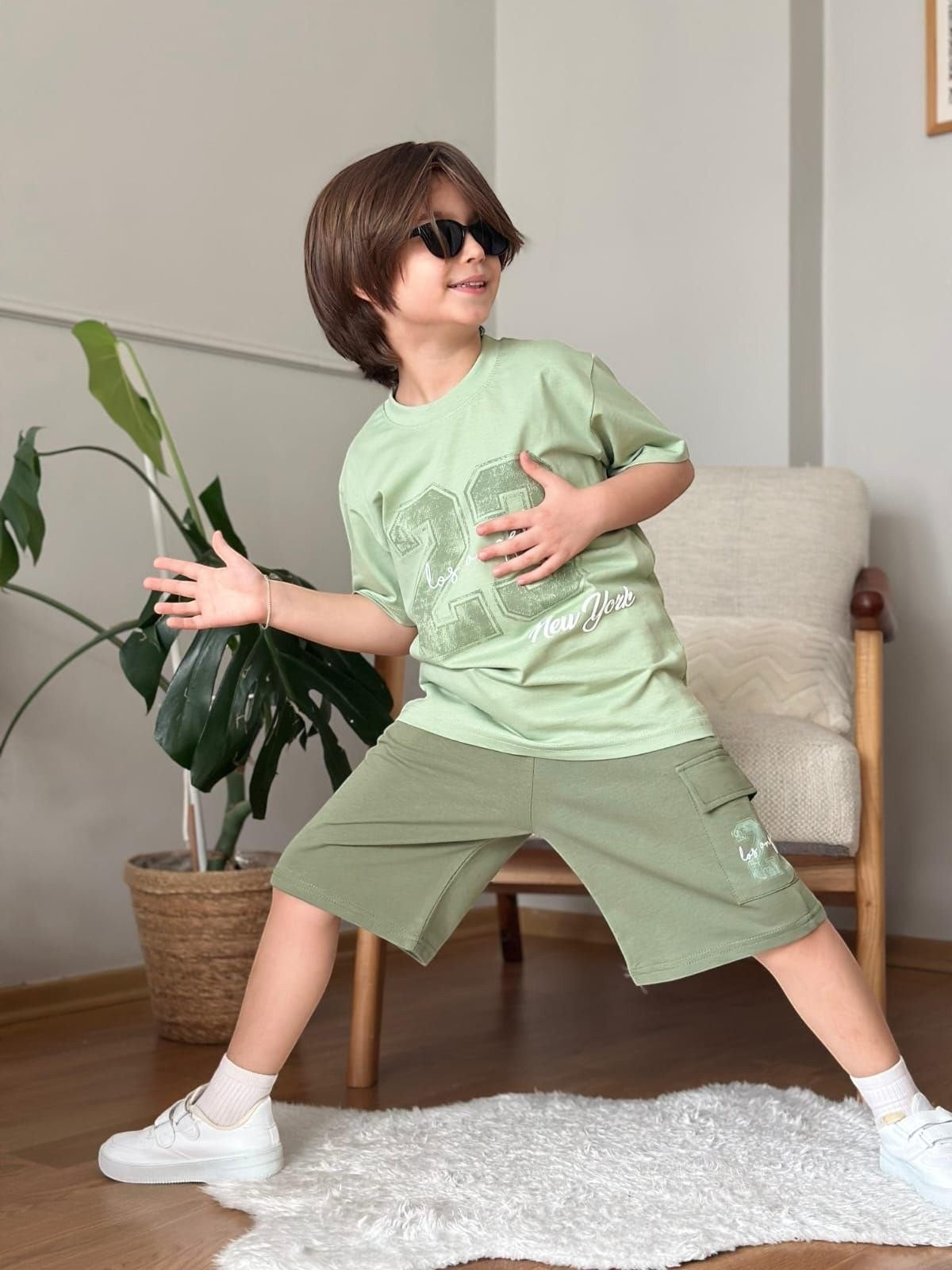 The Nile Luxuries boys sage green graphic t-shirt and cargo shorts set with sunglasses, worn by a young boy.