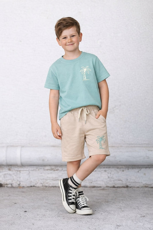 Young boy wearing The Nile Luxuries sage green t-shirt and beige shorts with palm tree embroidery for summer
