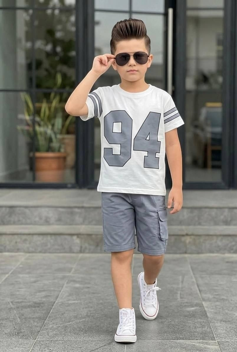 Boy wearing The Nile Luxuries varsity-style white t-shirt with 94 print and grey cargo shorts with sneakers.