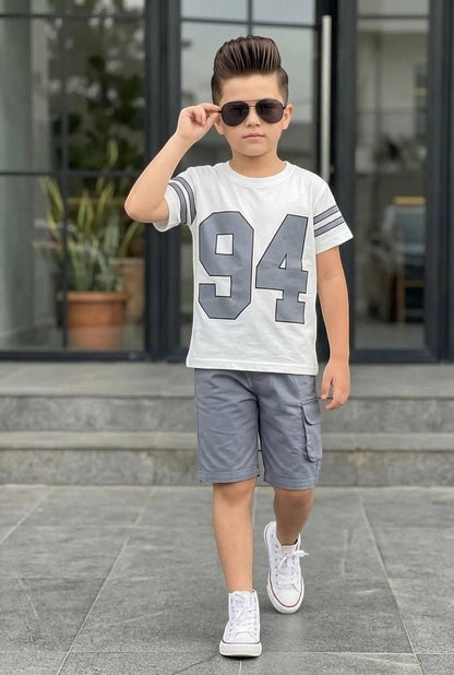 Boy wearing The Nile Luxuries varsity-style white t-shirt with 94 print and grey cargo shorts with sneakers.