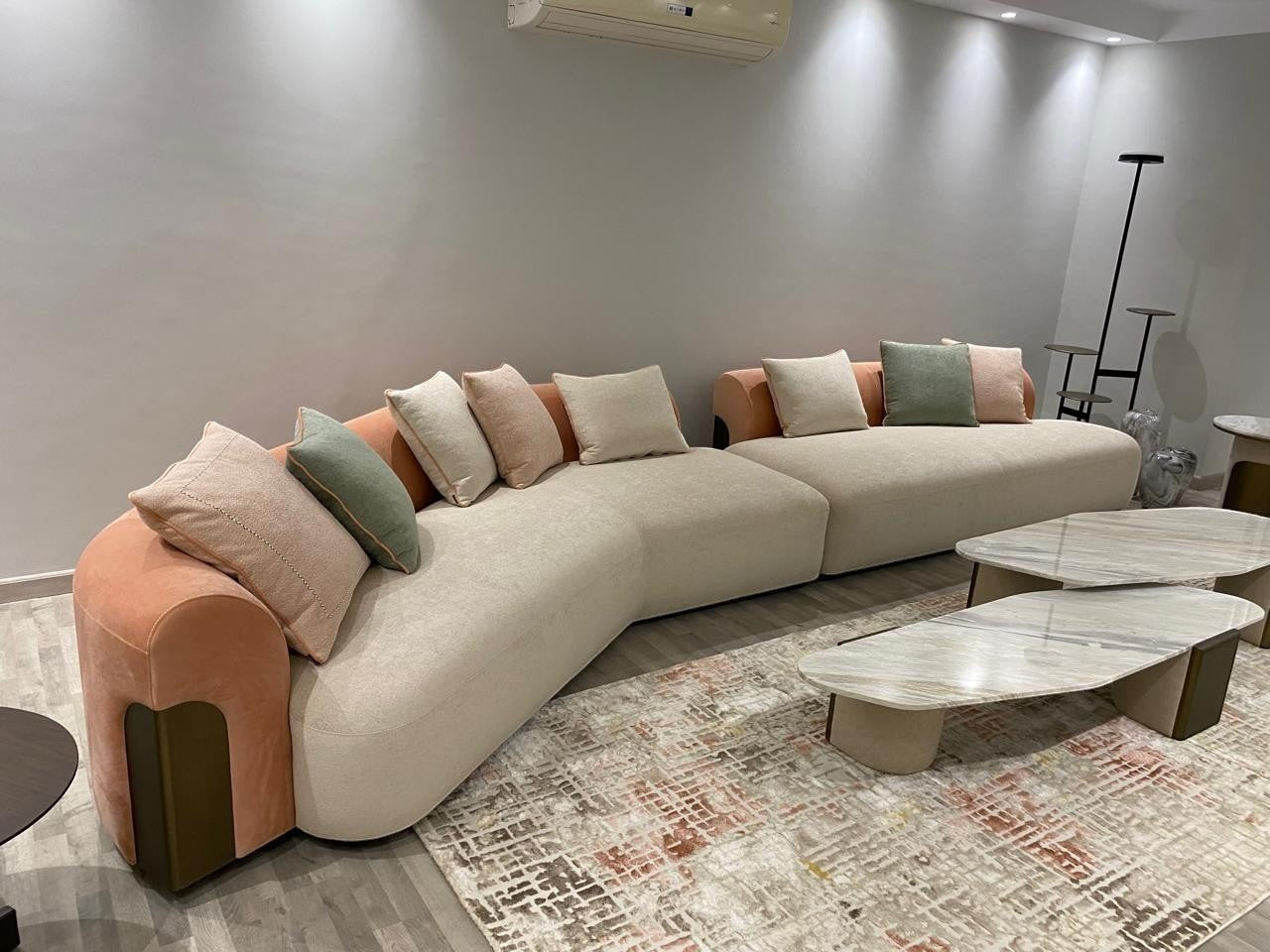 The Nile Luxuries contemporary cream sectional sofa with curved silhouette, rounded arms, and peach accents. Includes throw pillows.