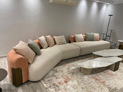 The Nile Luxuries contemporary cream sectional sofa with curved silhouette, rounded arms, and peach accents. Includes throw pillows.