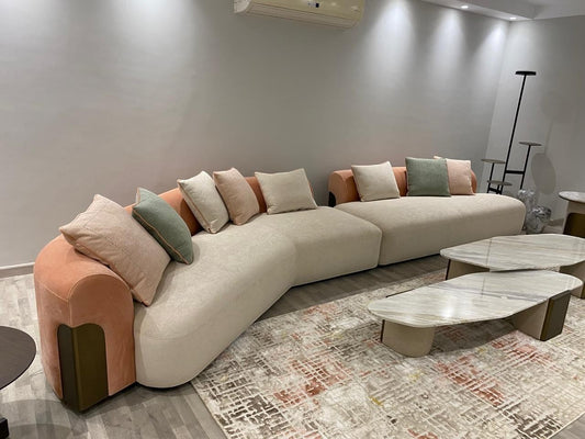 The Nile Luxuries contemporary cream sectional sofa with curved silhouette, rounded arms, and peach accents. Includes throw pillows.