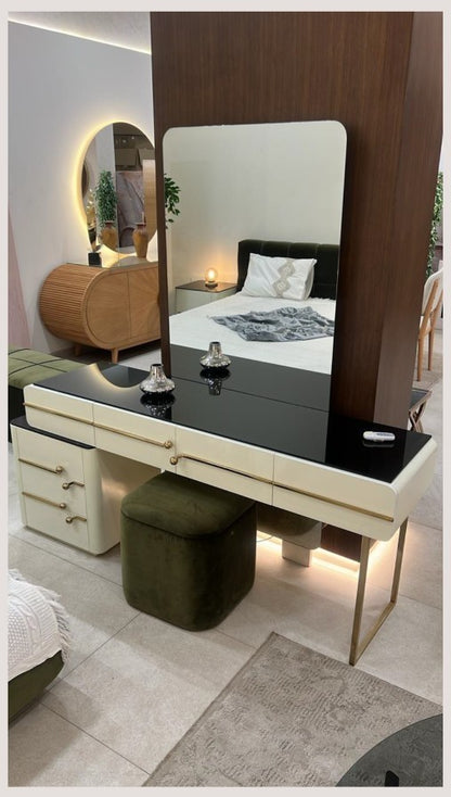 The Nile Luxuries high-gloss cream vanity with black glass top, gold hardware, and olive green ottoman. Features drawers and sleek legs.