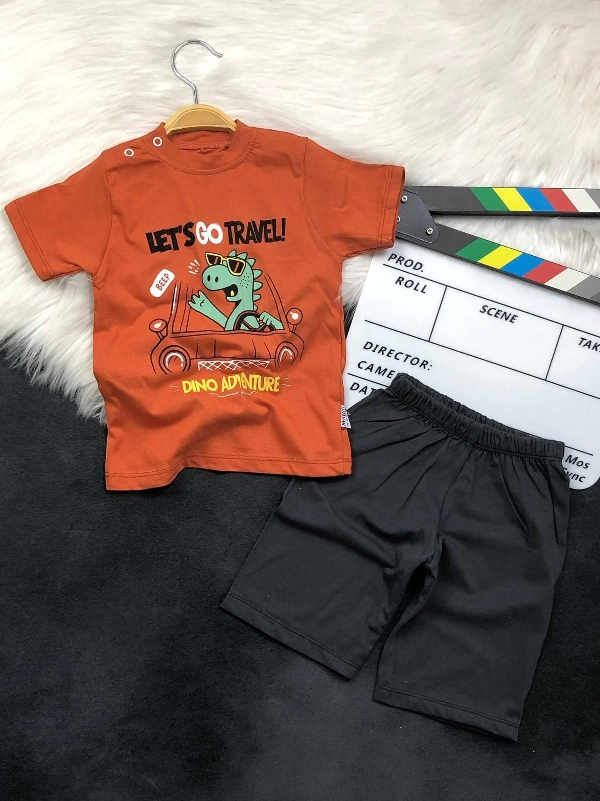The Nile Luxuries toddler boy outfit with an orange dinosaur graphic t-shirt and black shorts on a white fur rug.