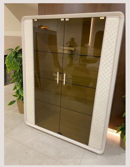 The Nile Luxuries display cabinet with smoked glass doors, cream quilted panels, and gold hardware. Modern furniture.