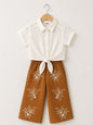 The Nile Luxuries off-white textured short-sleeve collared shirt tied at front, paired with brown wide-leg cropped pants with white floral embroidery.