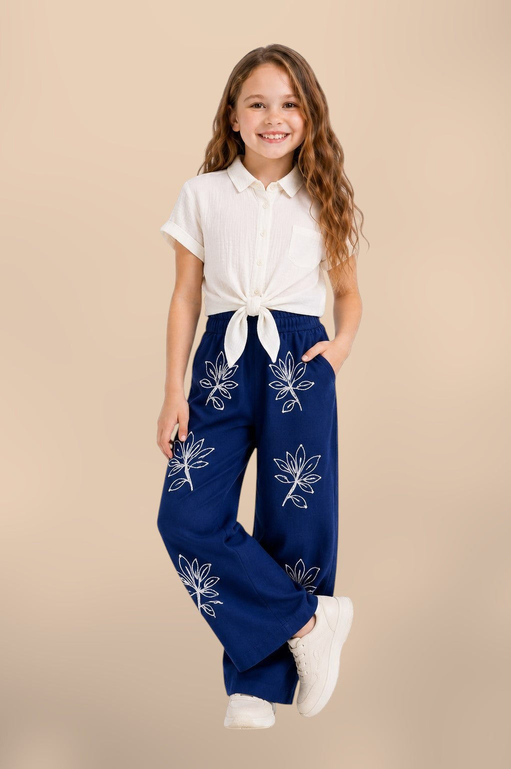The Nile Luxuries girls' off-white textured shirt tied at front, paired with navy blue wide-leg pants embroidered with white floral pattern.