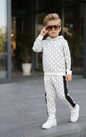 A young boy wearing The Nile Luxuries white and black geometric print hoodie and jogger lounge set with sunglasses.