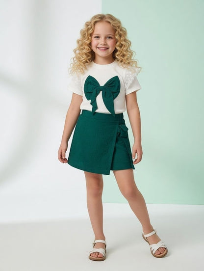 The Nile Luxuries girls' white ribbed top with lace sleeves and green bow paired with a matching green wrap skirt.