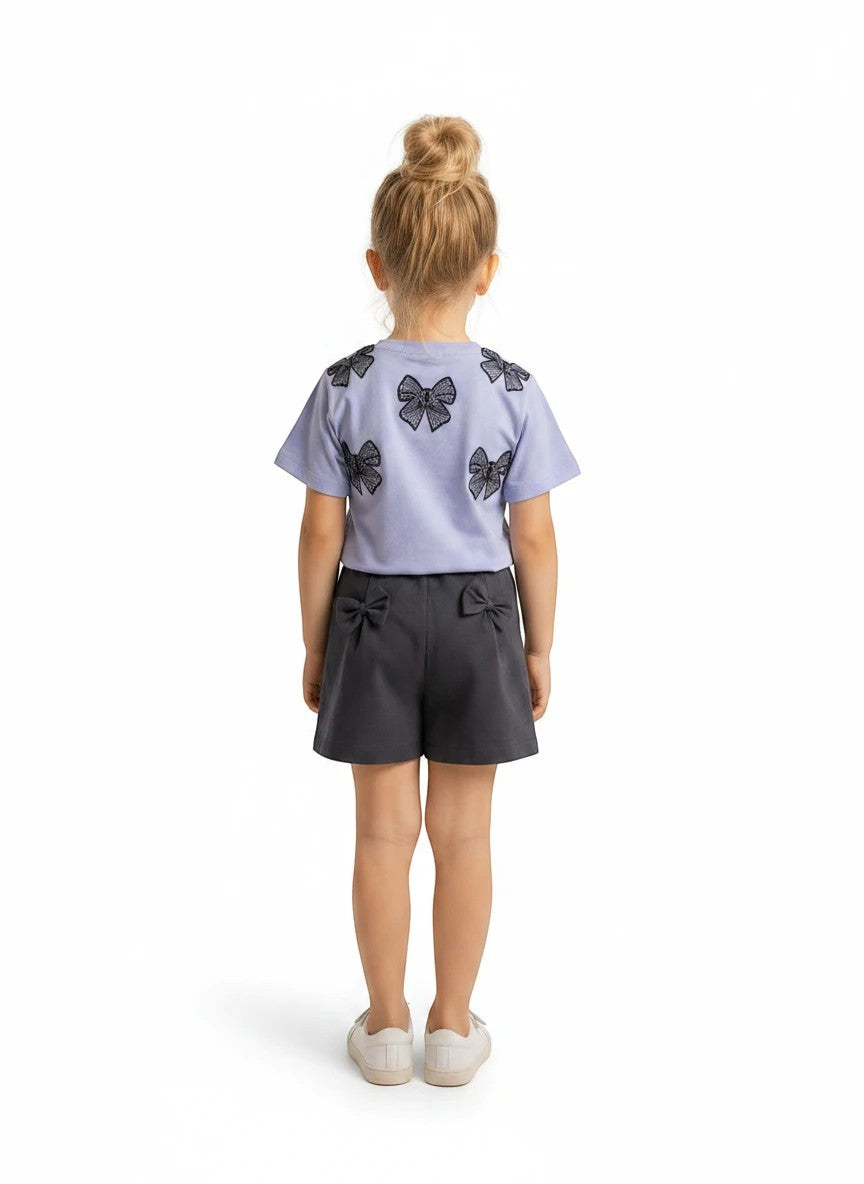 The Nile Luxuries girls casual summer outfit with a light purple bow-print t-shirt and grey shorts, back view.