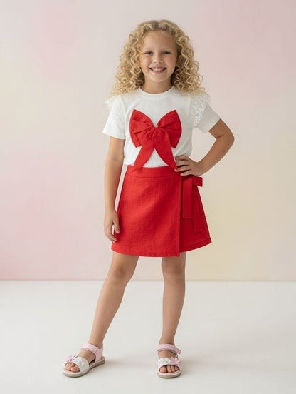 The Nile Luxuries girls white ribbed top with lace sleeves and red bow paired with a matching red wrap skirt