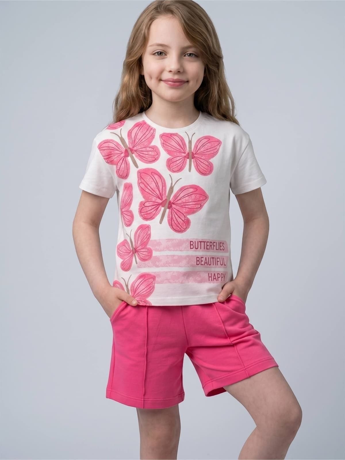 Young girl wearing a The Nile Luxuries white t-shirt with pink butterfly graphics and matching pink shorts.