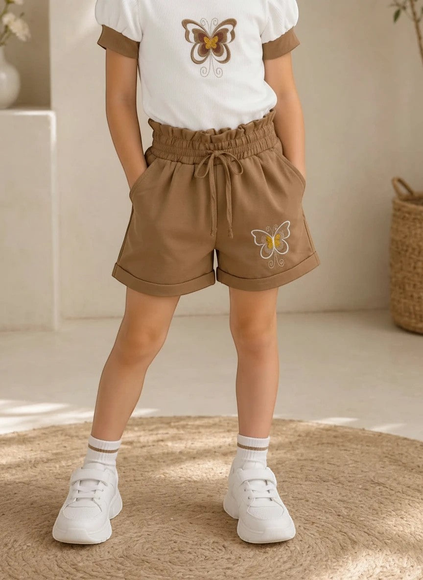 The Nile Luxuries girls white ribbed puff-sleeve top and brown paper-bag waist shorts set with butterfly embroidery.