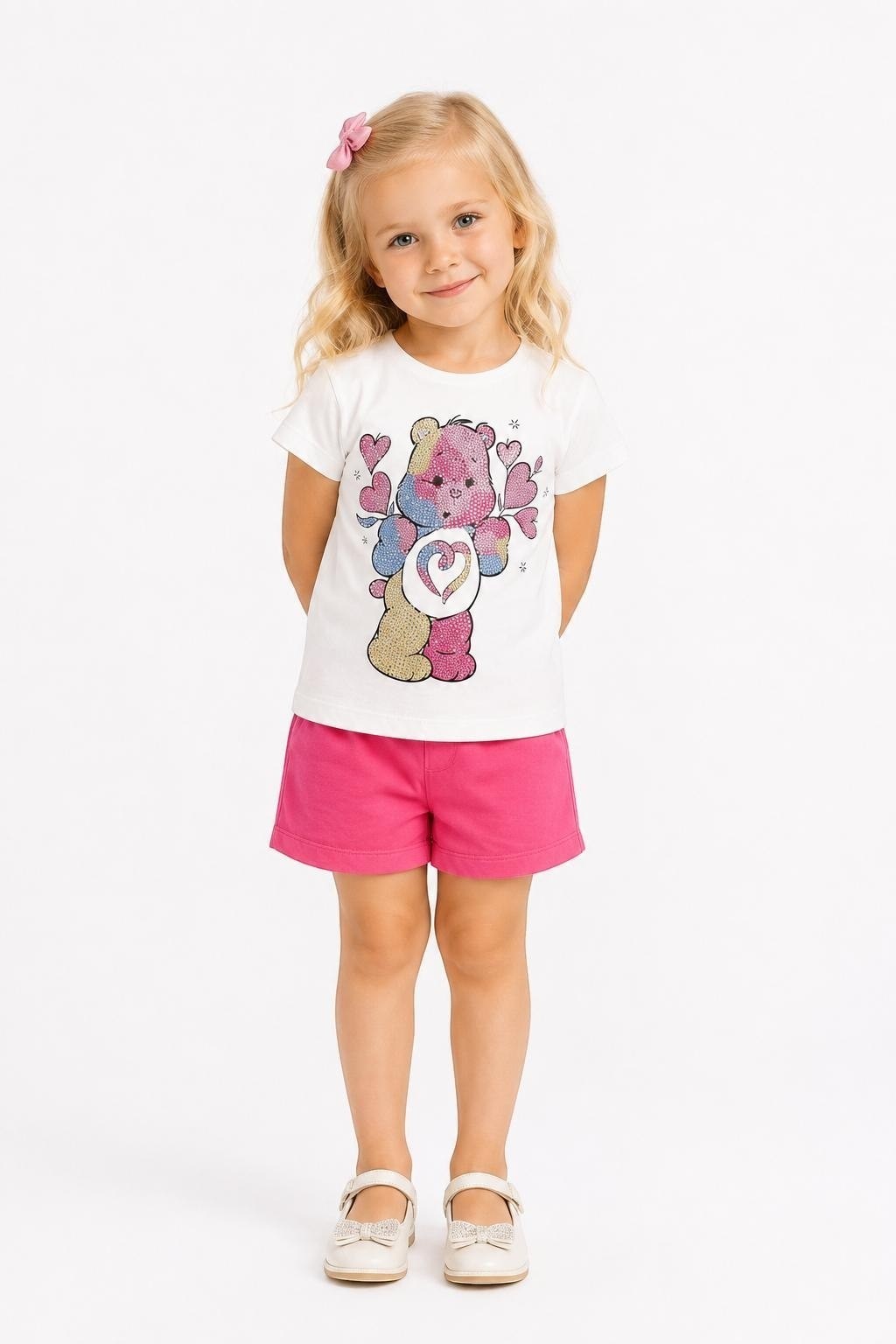 Young girl wearing a The Nile Luxuries white Care Bears graphic tee and pink shorts with a matching hair bow.