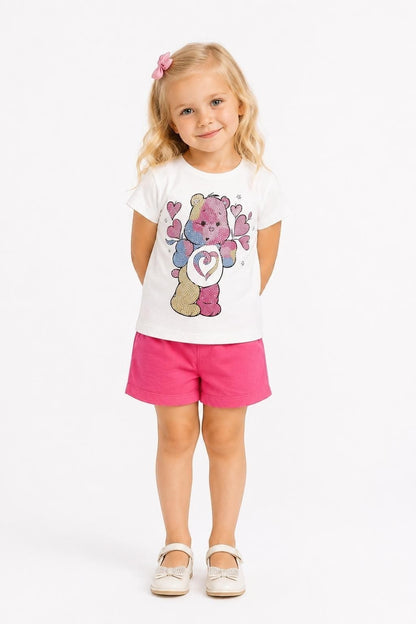 Young girl wearing a The Nile Luxuries white Care Bears graphic tee and pink shorts with a matching hair bow.