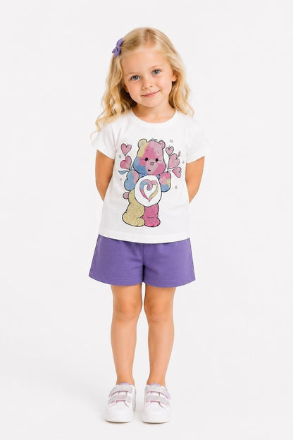 Young girl wearing a The Nile Luxuries white Care Bears graphic tee and purple shorts with white sneakers.